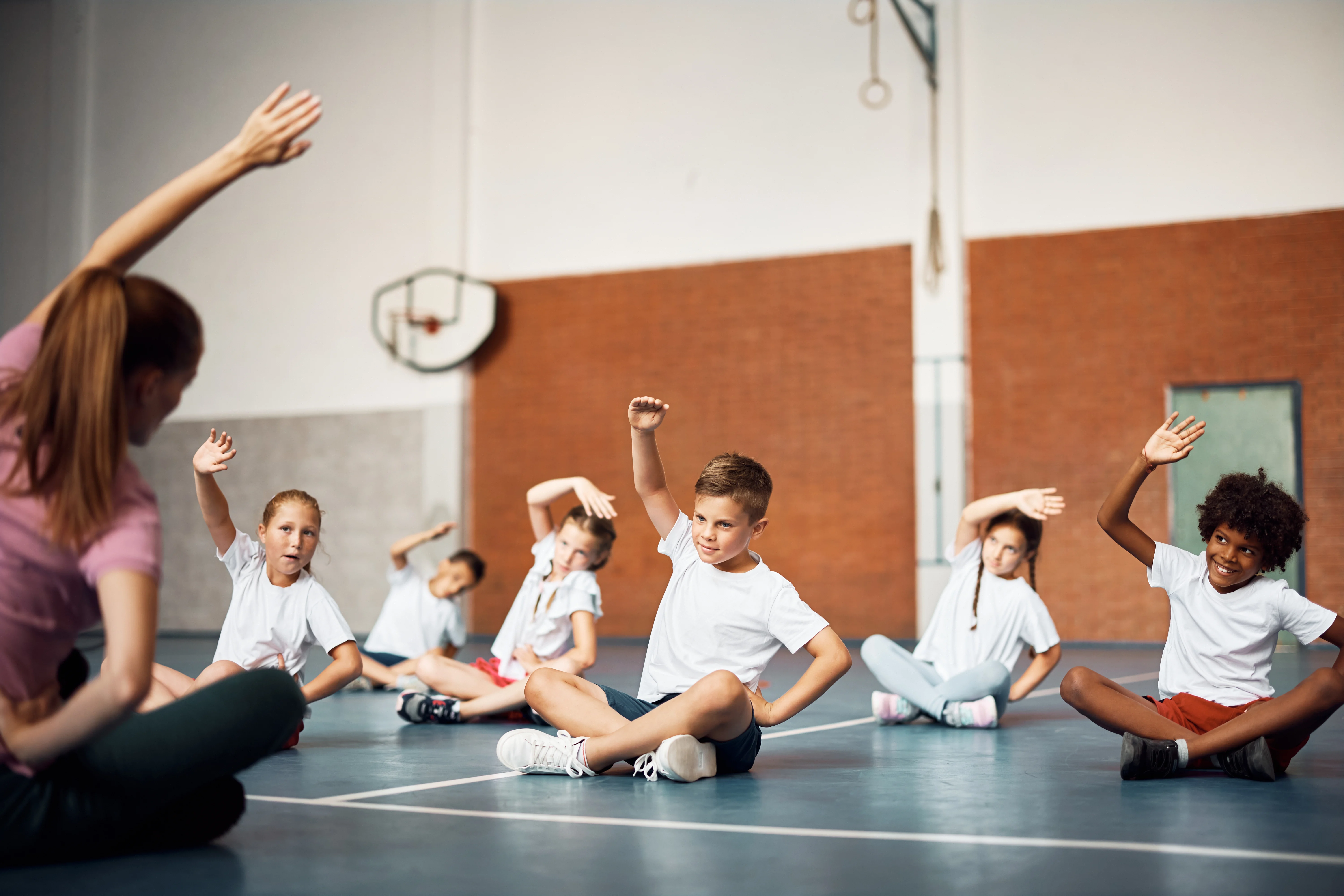 Elementary school children exercising with PE teacher at school gym.